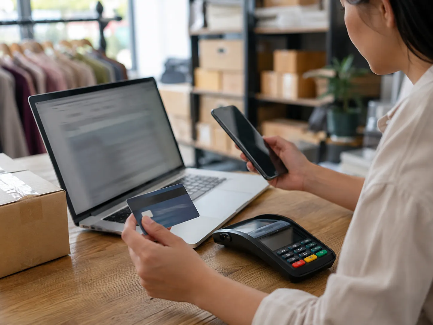 Small business owner reviewing online and card-not-present payment activity with a laptop and card terminal.