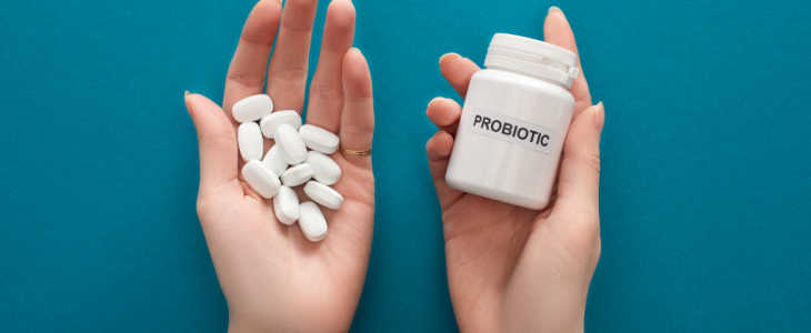cropped view of woman holding white probiotic container and pills in hands on blue background