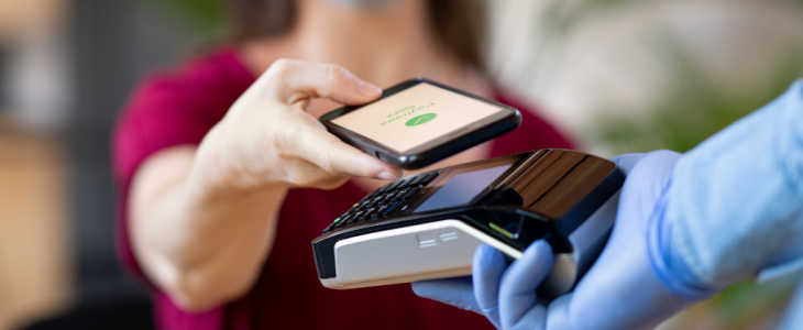Close up hand of customer paying with smartphone. Cashier hand holding credit card reader machine and wearing protective disposable gloves at bar counter, while client holding phone for NFC payment. Woman wearing face mask while paying bill with mobile phone during Covid-19 pandemic.